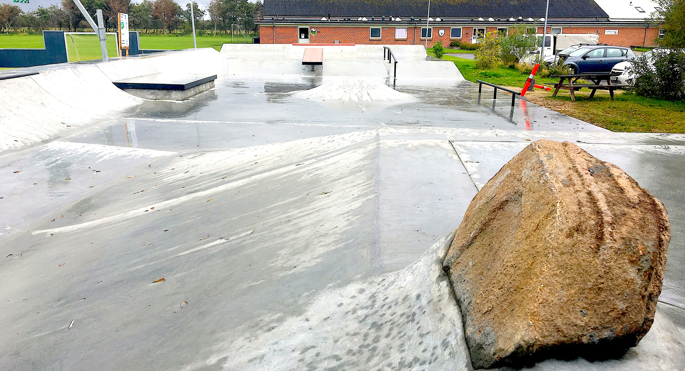 Billedet viser en skatepark i beton med en stor natursten i forgrunden