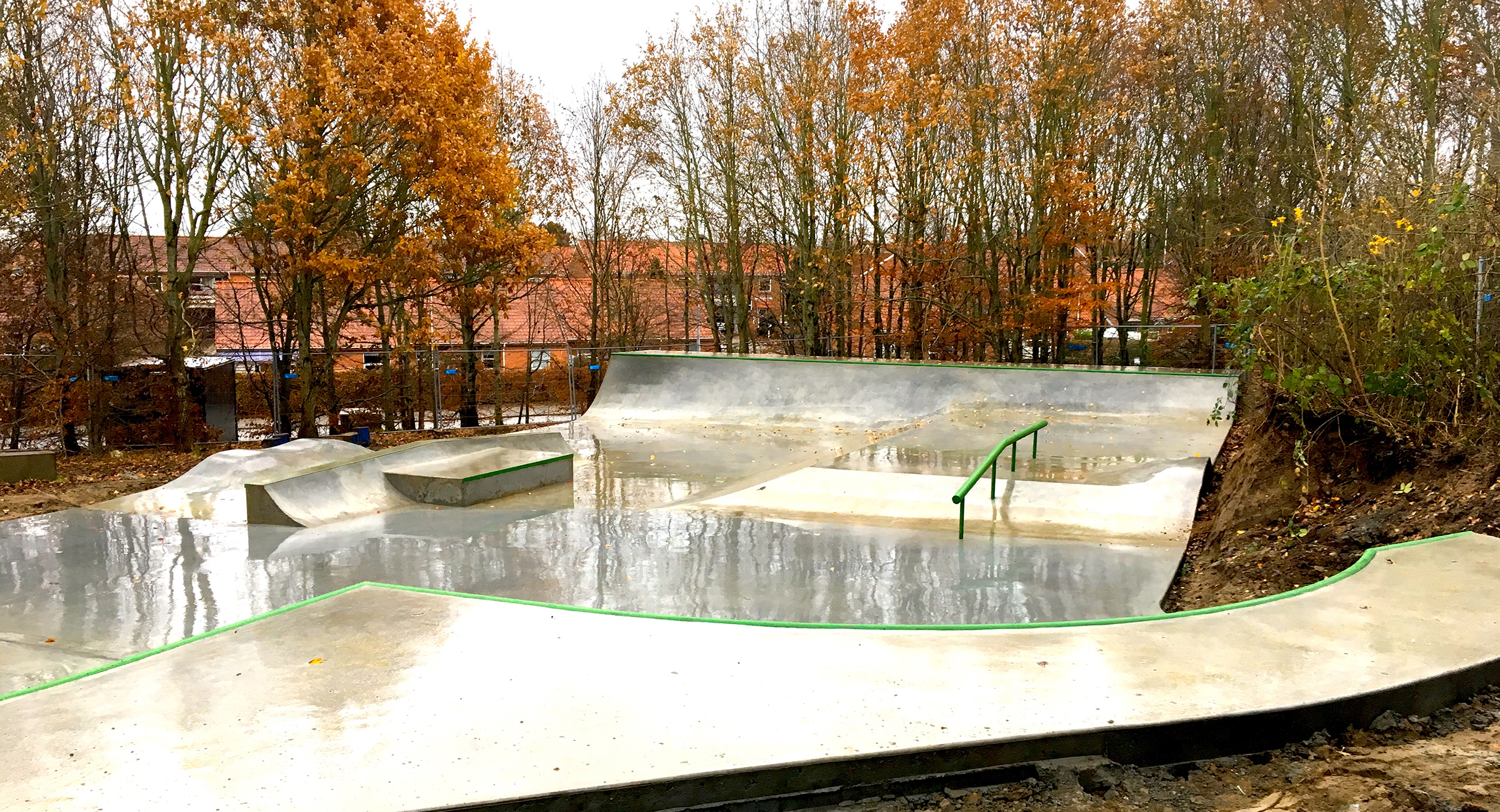 Billedet viser en lille skatepark i beton med grønne metalelementer