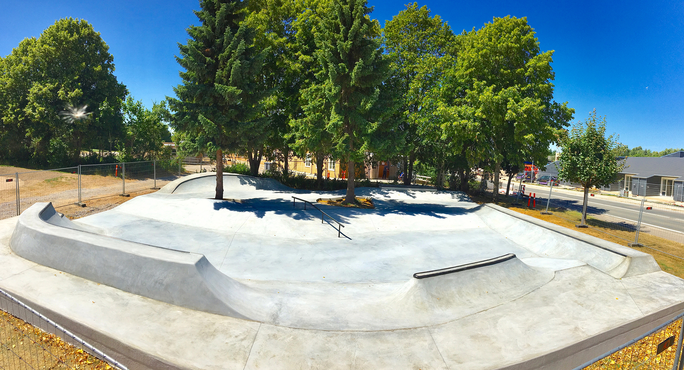 Billedet viser en beton skatepark med voksne træer i midten og siderne