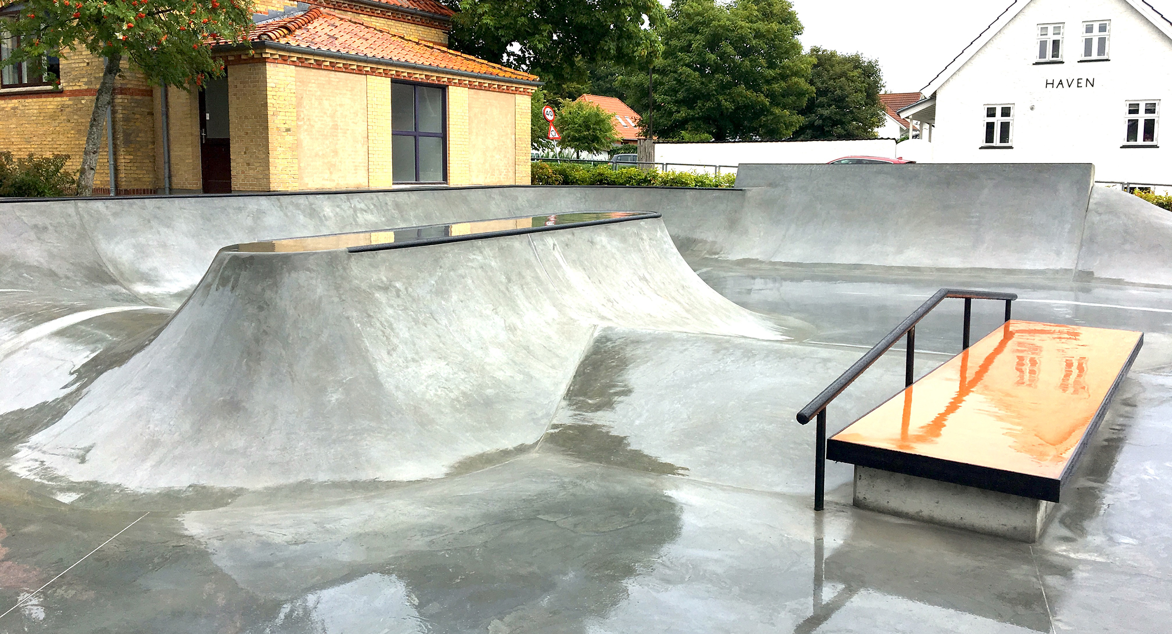Billedet viser en skaterampe i beton med gelænder og en curb ved siden af