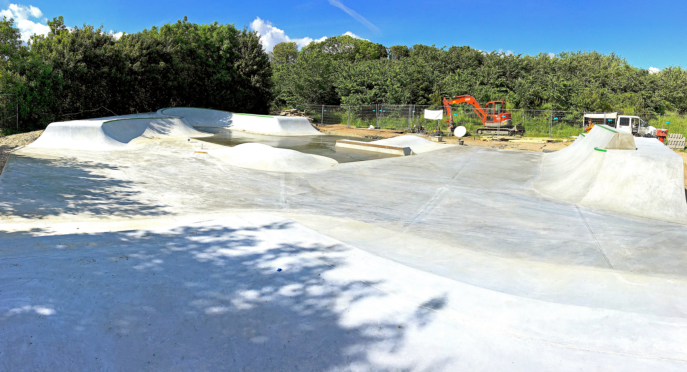 Billedet viser en skatepark i beton med et enkelt vådt, nystøbt område tilbage