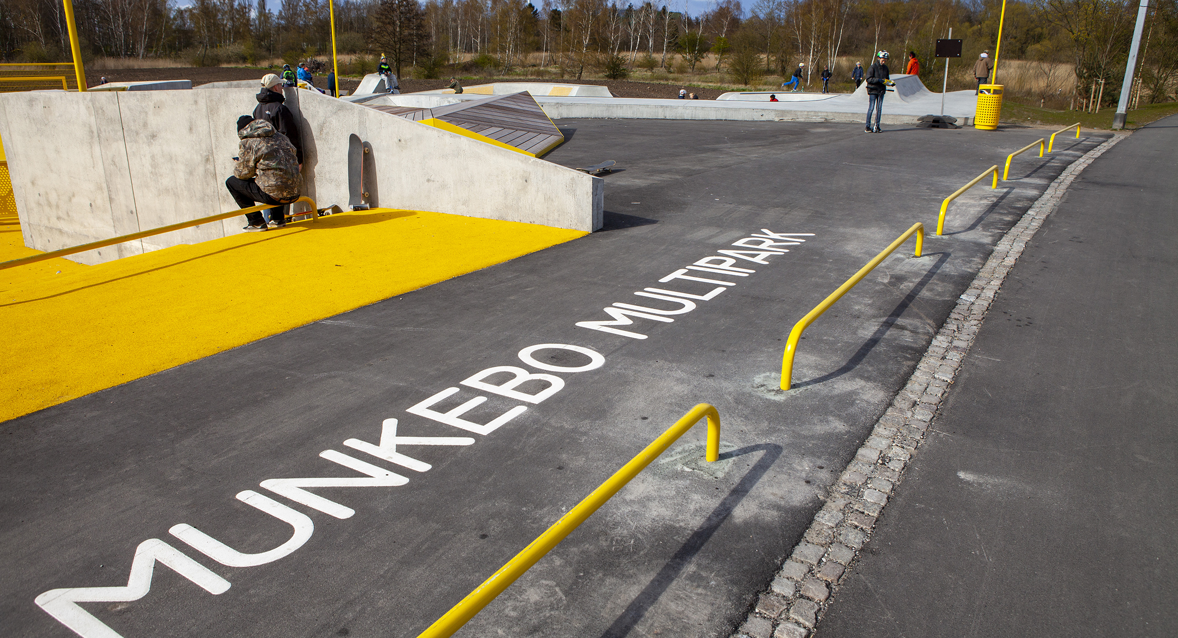 Gul-malede metalgelændre afgrænser et asfalteret område. På asfalten står der Munkebo Multipark