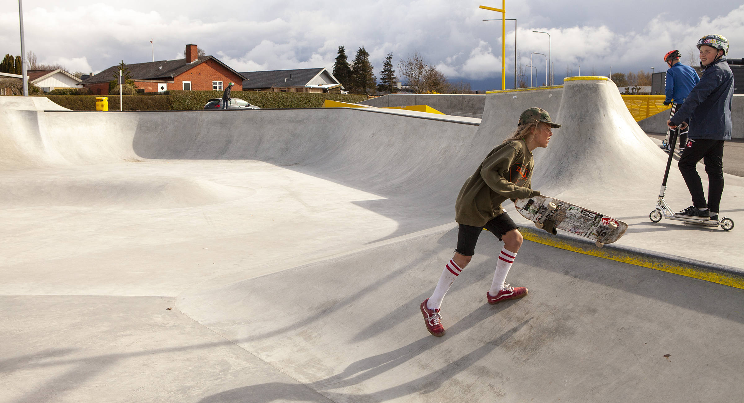 En skateboarder og to drenge på løbehjul bruger en skatepark i beton i Munkebo