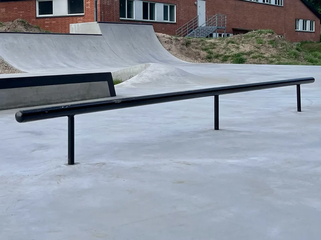 Nærbillede af et sort rail i Svinninge Skatepark. Bagved ses et lille speed bump og en stor quarter i beton.