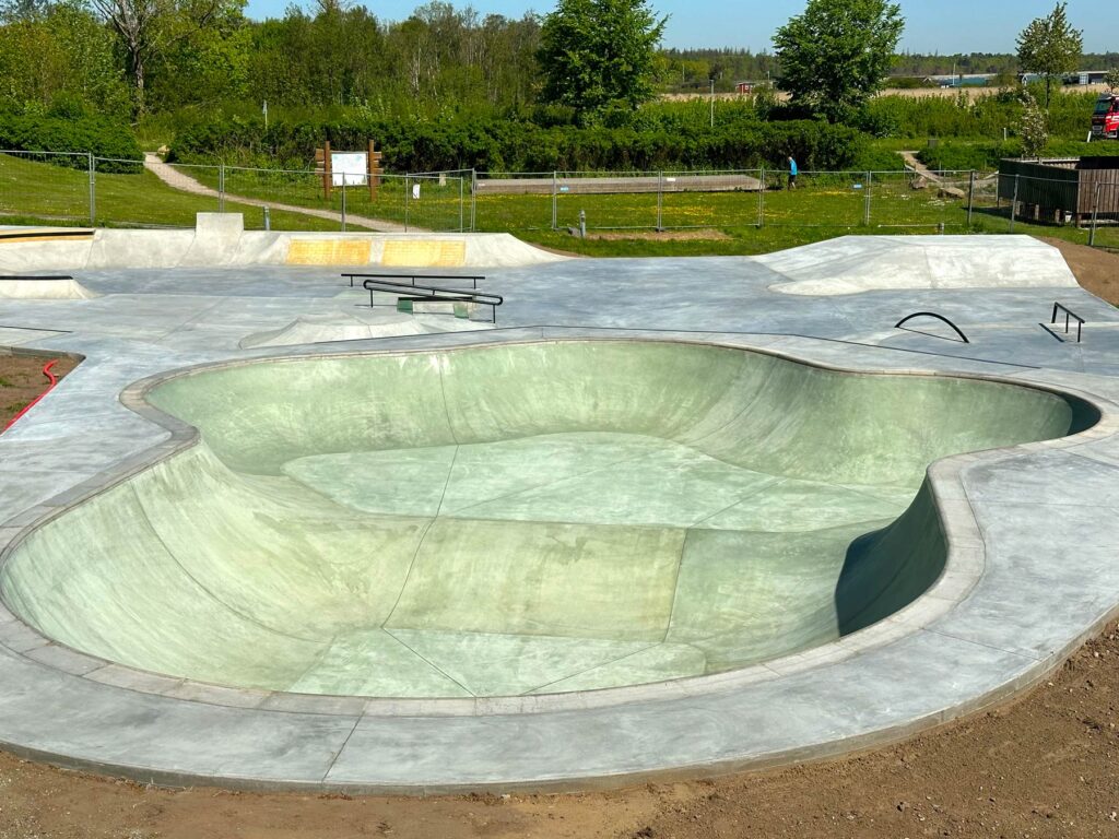 Den grønlige beton bowl i Juelsminde Skatepark har en lav og en dyb ende og tre hips