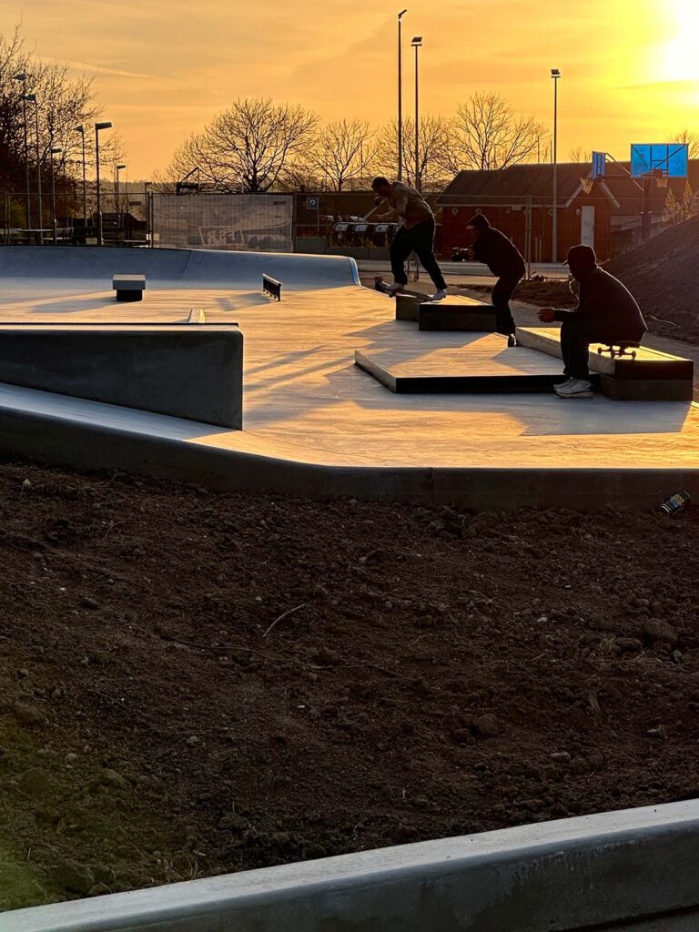 Solnedgang over Middelfart Skatepark, hvor skatere er i gang med at teste den nye buede curb